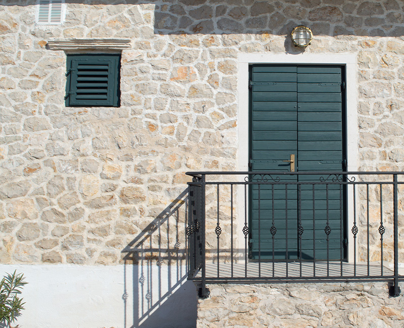 stone house facade with green door and window features balcony with iron railing natural light entrance eight rustic design elements