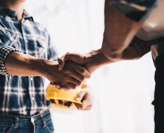 two individuals shaking hands in a business agreement wearing plaid shirt and holding a hard hat partnership symbolizes teamwork and success in 7 key areas