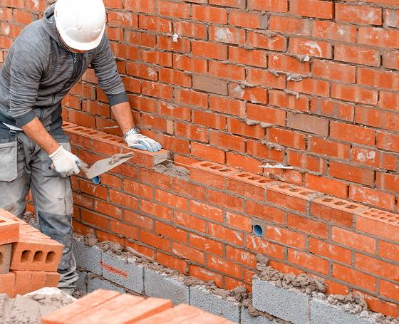 construction worker laying brick with gloves on a site using 9 bricks per row